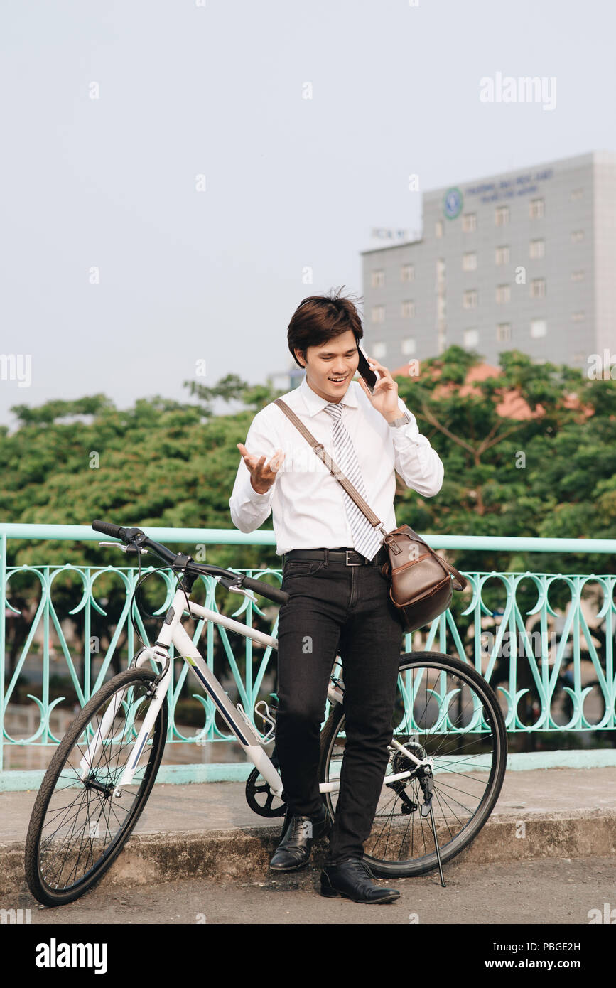 Portrait d'un étudiant parlant au téléphone et de l'article par un vélo isolé sur fond blanc Banque D'Images