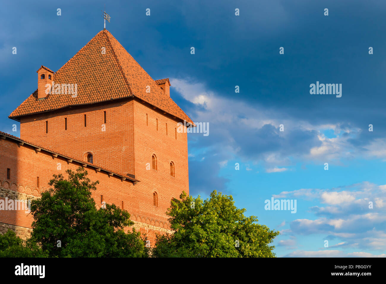 Une puissante tour du château de Lida en brique et pierre rouge allumé avec le soleil contre un beau ciel d'orage, mais le Bélarus Banque D'Images