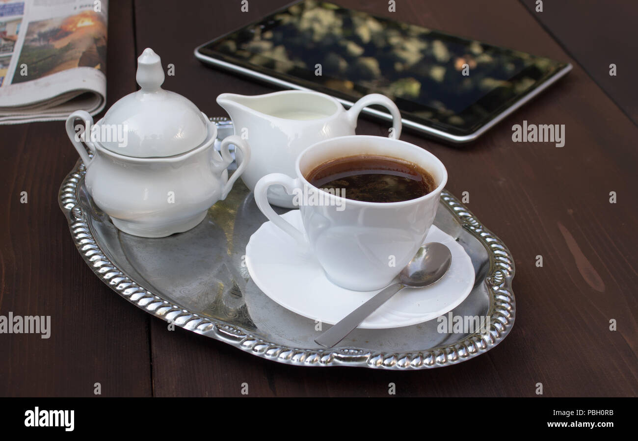 Sur la table en bois braun journal, comprimé, plaque, capuchon avec soucoupe et cuillère, sucrier, pot à lait et - concept de pause café Banque D'Images