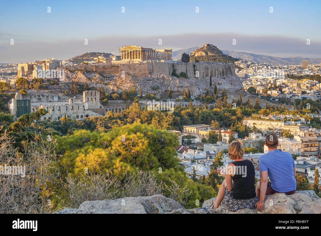 Couple regard la merveilleuse vue de la colline Filopappou en regardant vers l'acropole d'Athènes au coucher du soleil. L'Attique, la Grèce, l'Europe. Banque D'Images