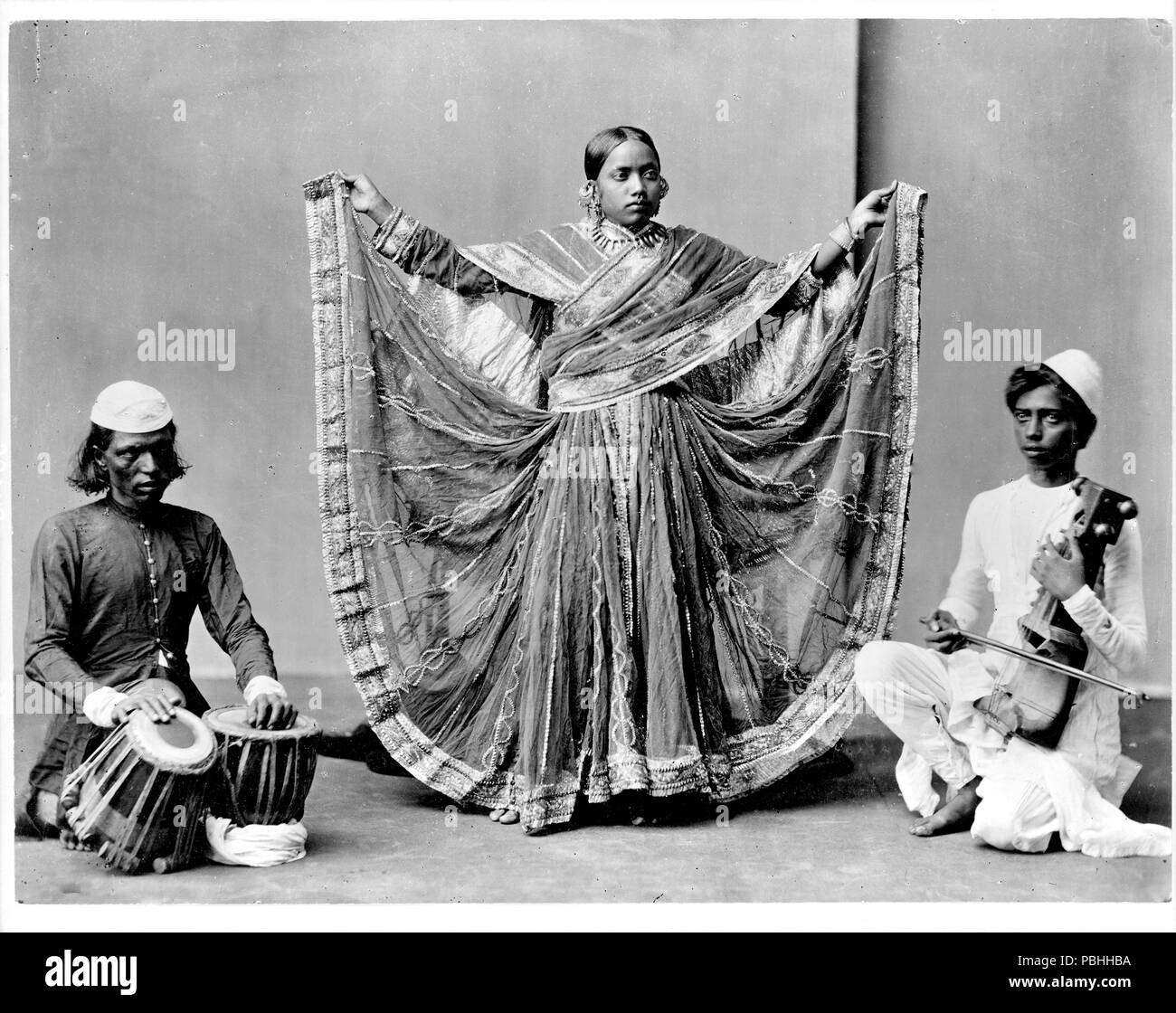 Photo montre une danseuse debout entre deux musiciens, l'un avec la batterie et l'autre avec un instrument à cordes. Nautch Girl - 1900 Banque D'Images