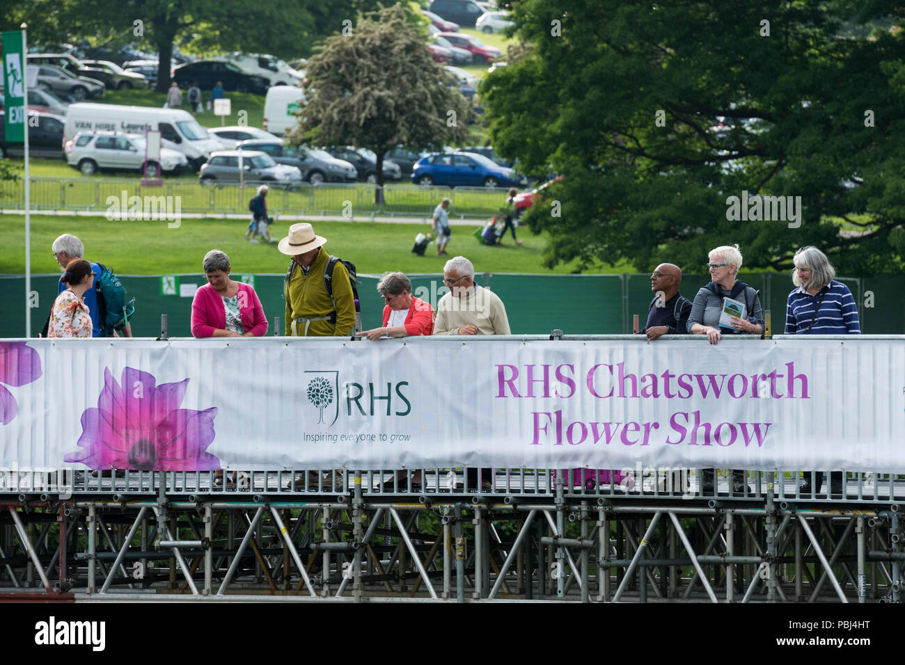 Showground visiteurs à Chatsworth RHS Flower Show, debout par bannière promotionnelle et à la recherche, au pont de la rivière temporaire - Derbyshire, Angleterre, Royaume-Uni. Banque D'Images