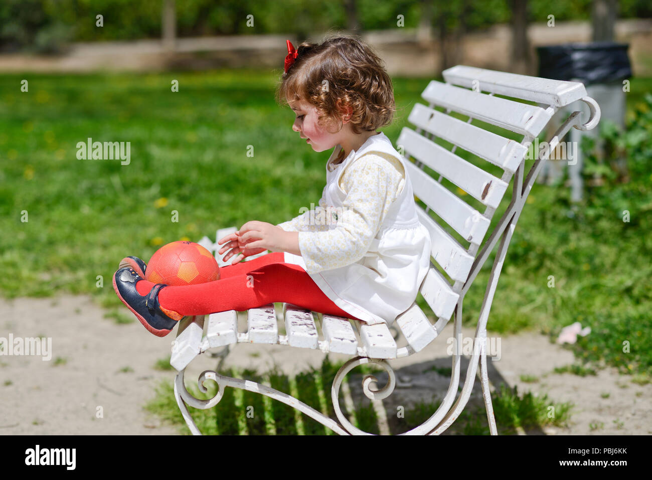 Adorable petite fille jouant avec une balle assise sur un banc de parc Banque D'Images