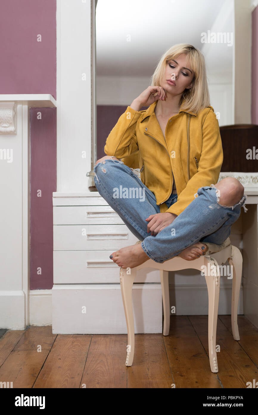 Femme blonde assise sur un tabouret devant une table portant une veste en  cuir jaune moutarde. La veste est décompressé Photo Stock - Alamy