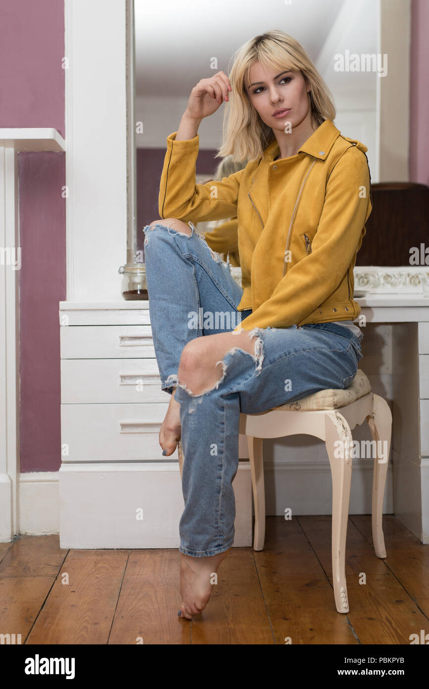Femme blonde assise sur un tabouret devant une table portant une veste en cuir  jaune moutarde. La veste est décompressé Photo Stock - Alamy