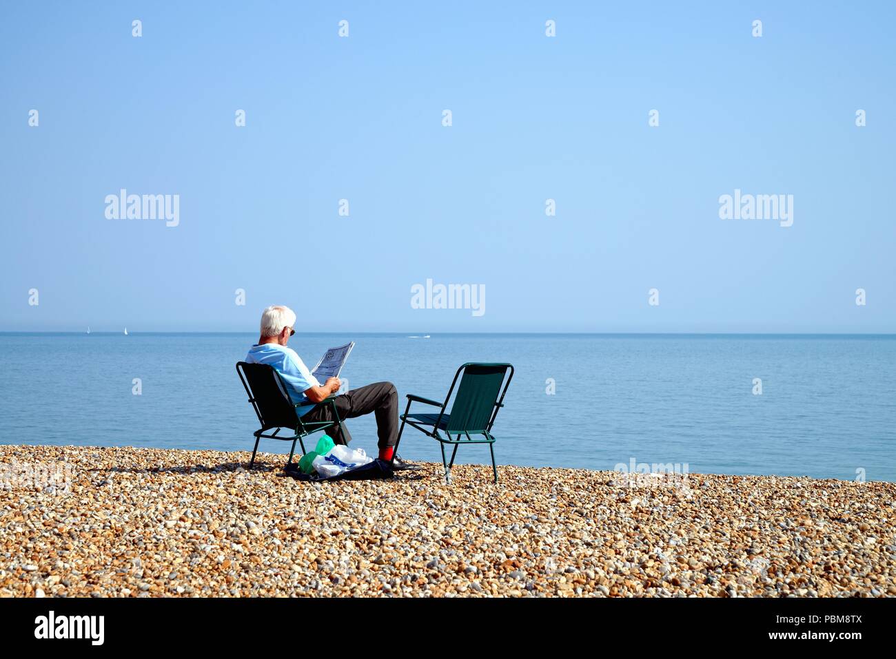 Personnes âgées homme blanc assis sur la plage à Hastings sur une chaude journée d'été, East Sussex England UK Banque D'Images