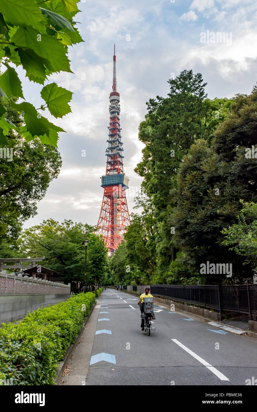 Vélo femme de l'appareil photo vers la Tour de Tokyo, l'aperçut à travers les arbres et un ciel nuageux ciel du soir Banque D'Images