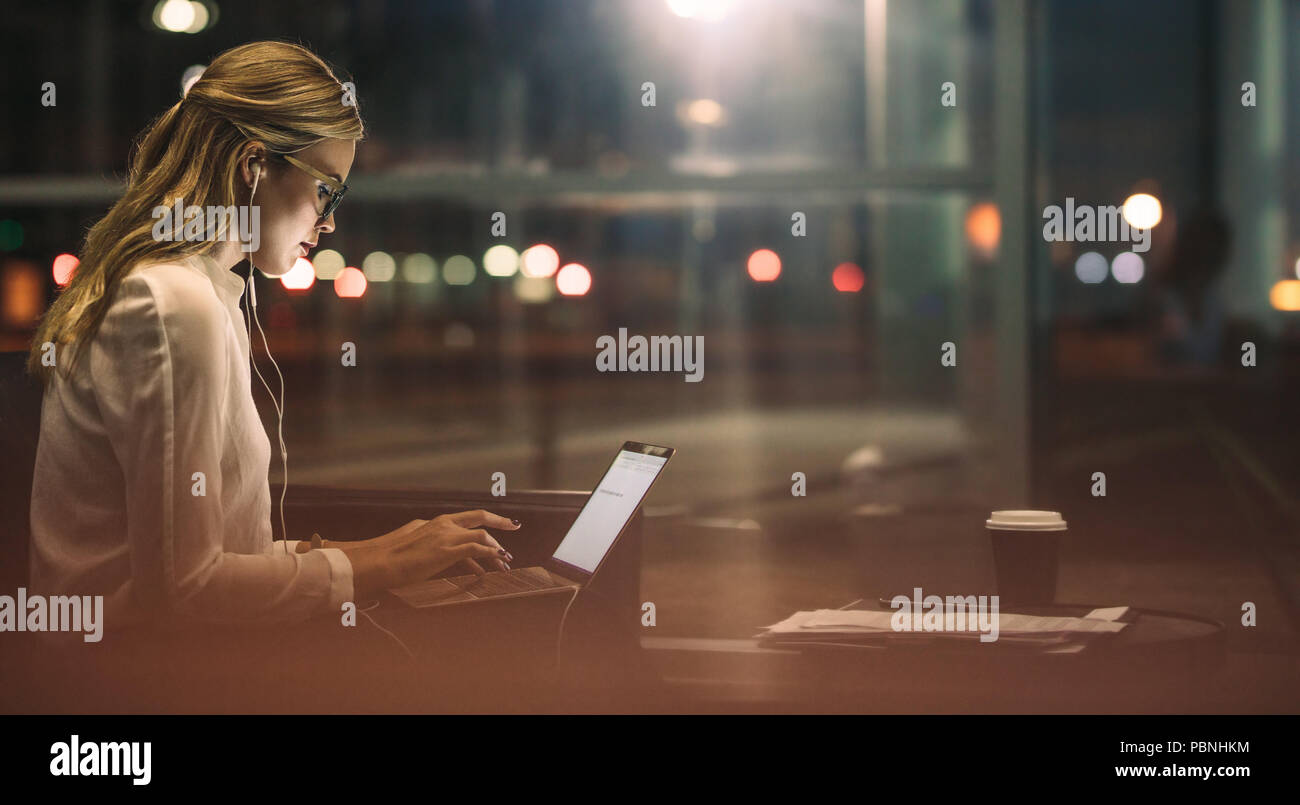 Side view of young female business professionnel travaillant sur un ordinateur portable. Faire des heures supplémentaires en femme d'office. Banque D'Images