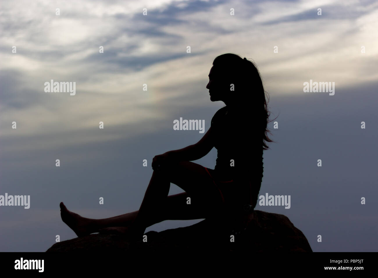 Silhouettes d'une femme assis sur le dessus du rock avec ciel crépusculaire au coucher du soleil. Banque D'Images