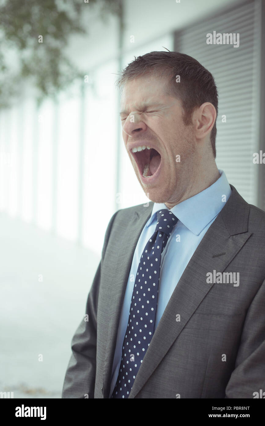 Homme de race blanche dans ses 30 ans vêtu d'un costume gris, chemise  déboutonnée et cravate desserrée, le bâillement Photo Stock - Alamy