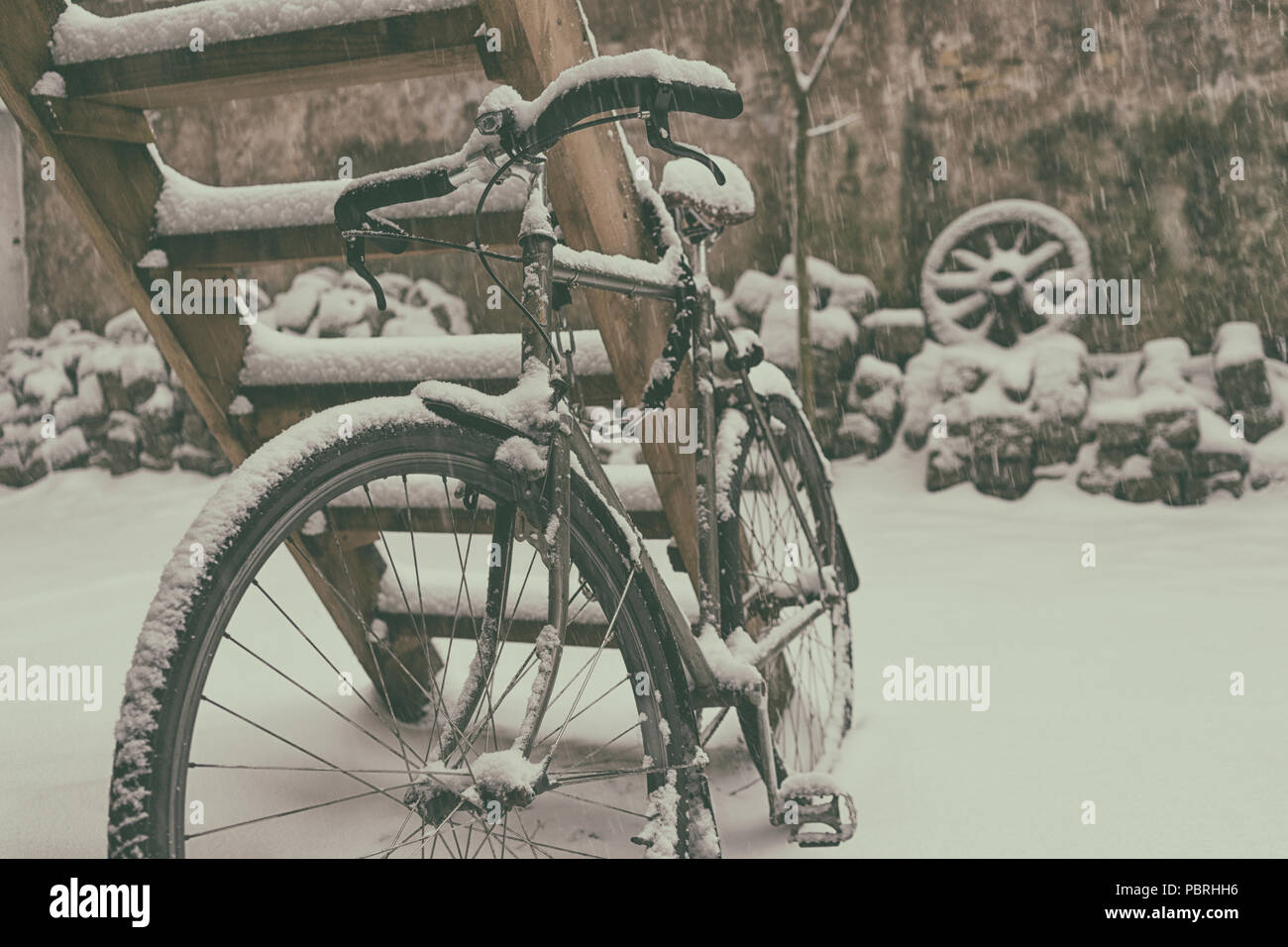 Vélo Vintage en hiver dans la neige enchaînés à une échelle en bois contre le mur avec une roue de chariot Banque D'Images