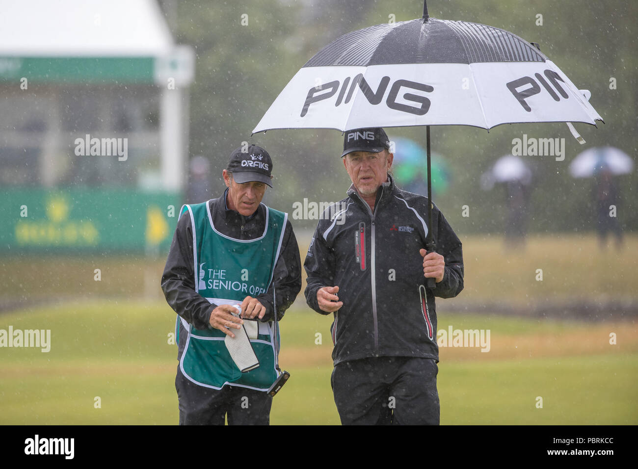 Miguel Angel Jimenez s'abrite de la pluie au 1er trou au cours de la quatrième journée de l'Open Senior au Old Course St Andrews. Banque D'Images