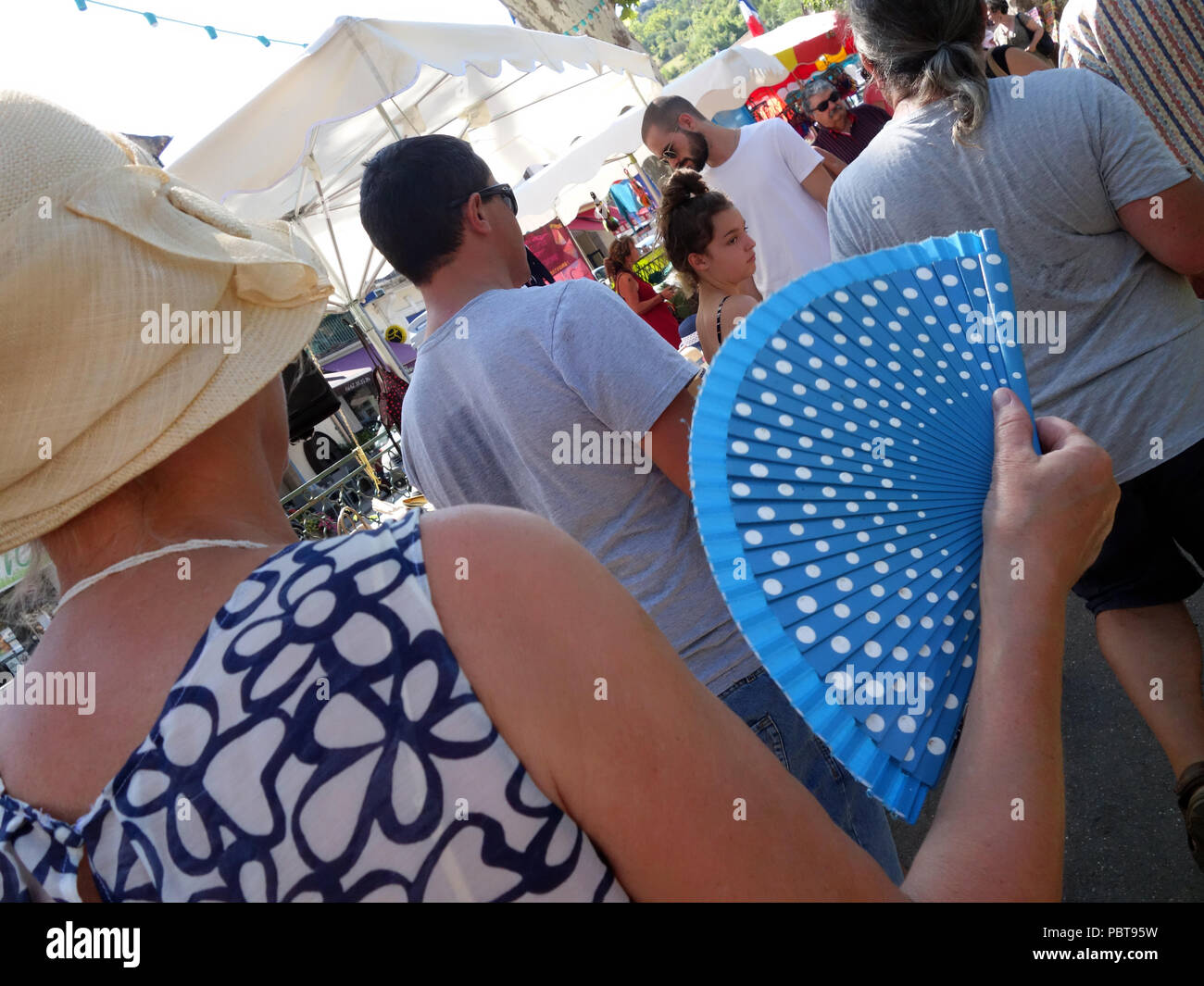 Woman fanning elle-même avec un ventilateur pliant bleu comme elle marche autour d'un marché de rue dans le sud de la France Banque D'Images