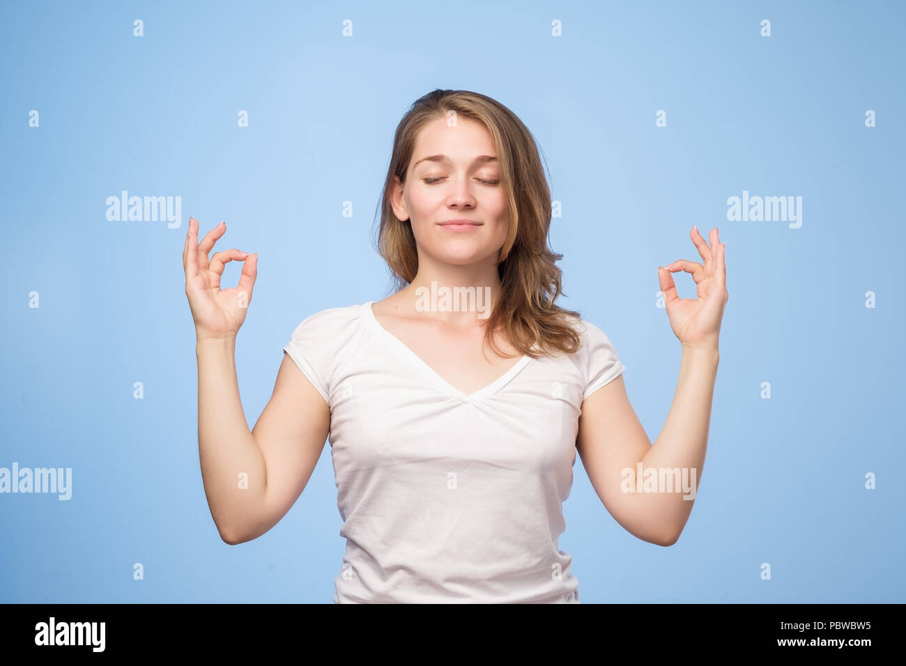 Permettez-être calme. Portrait de femme attrayante détendue avec les yeux fermés, sourire heureux, méditant avec propagation mains Banque D'Images