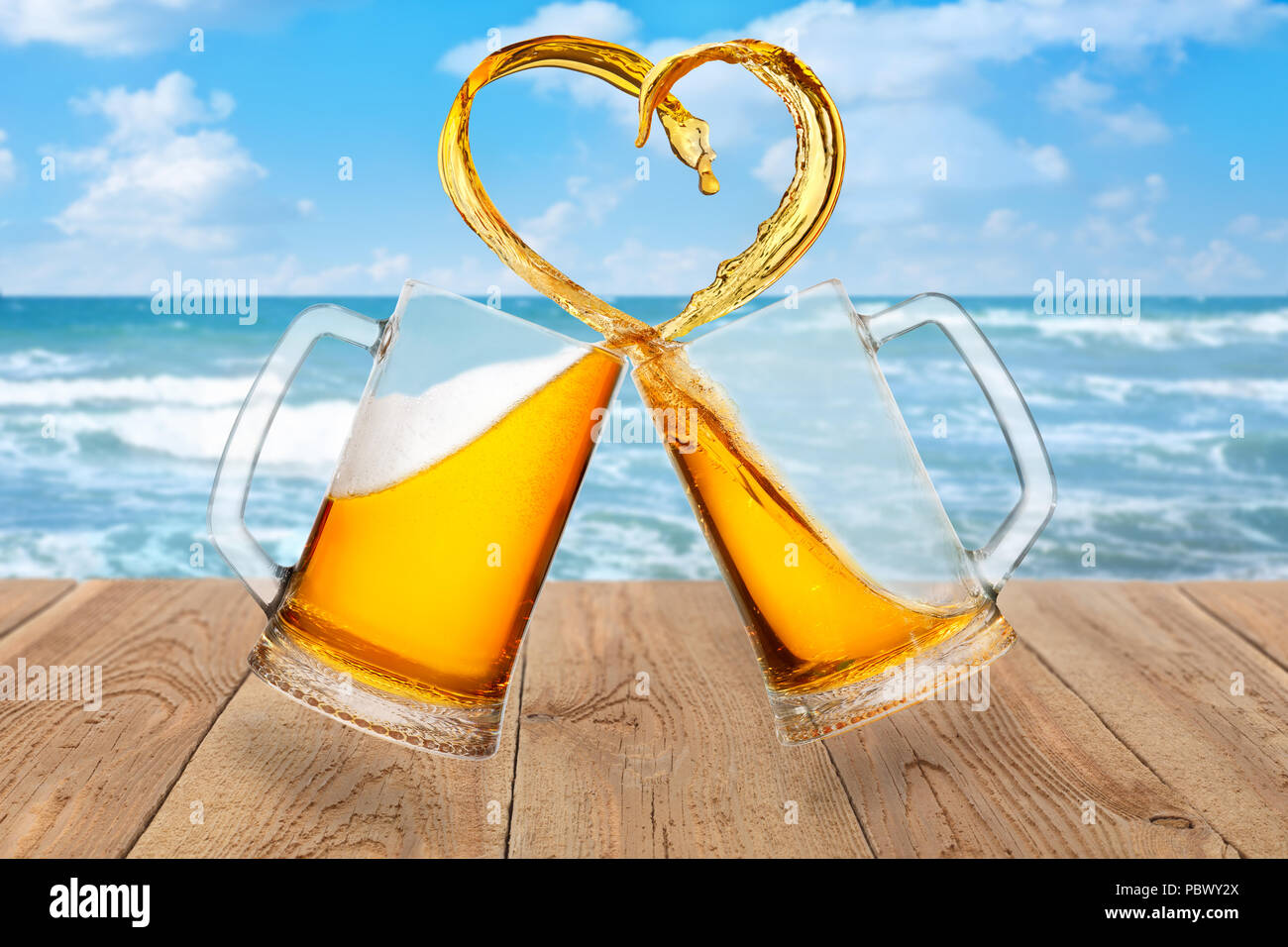 L'amour de la bière concept. Deux tasses en verre toasting et la création d'éclaboussure de forme de coeur sur fond de mer Banque D'Images