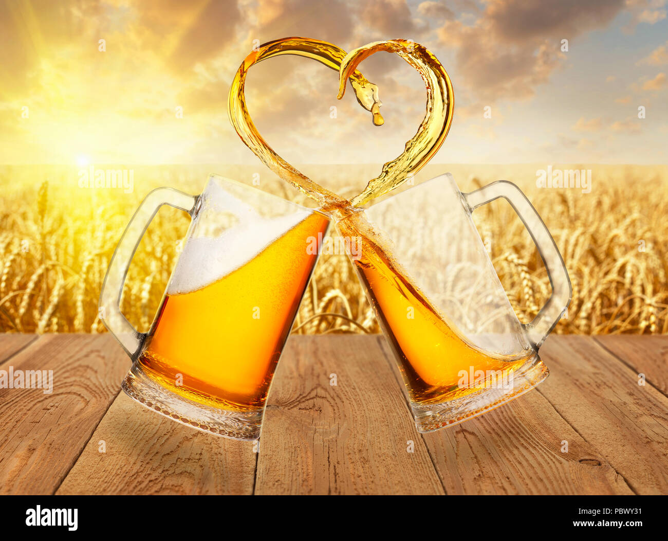 L'amour de la bière concept. Deux tasses en verre toasting et la création d'éclaboussure de forme de coeur sur fond de champ de blé mûr Banque D'Images