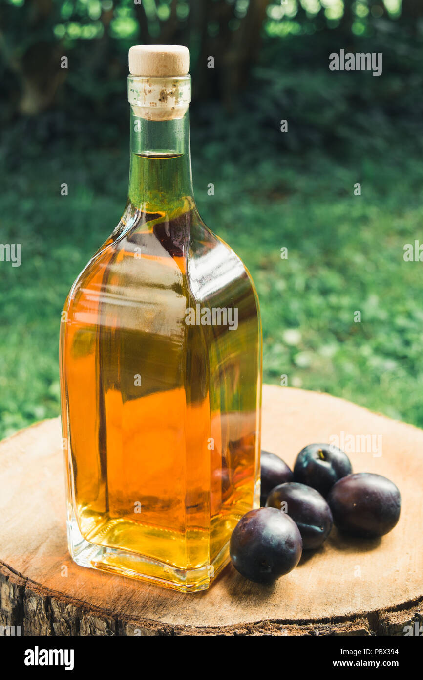 Eau-de-vie de prune (Slivovitz) dans le flacon en verre avec des prunes mûres sur une surface en bois. Banque D'Images