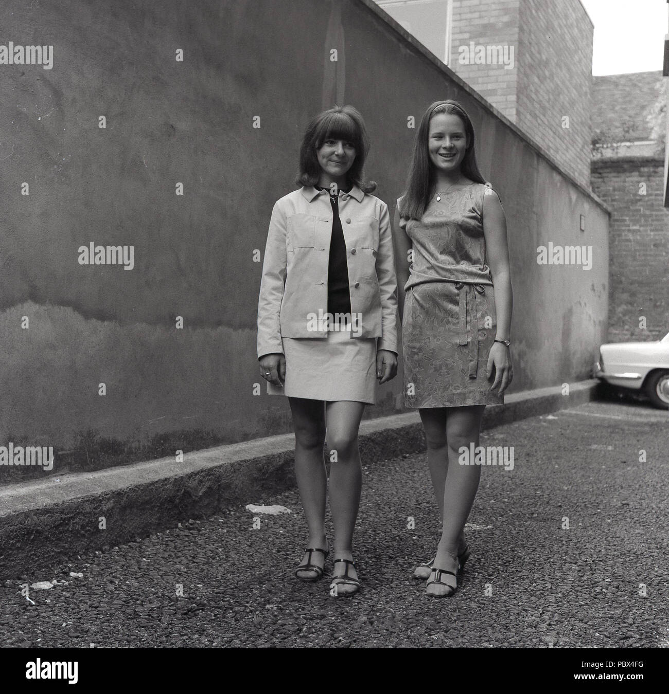 1964, historiques, deux jeunes femme debout portant l'extérieur de la journée de la mode féminine, England, UK. Banque D'Images