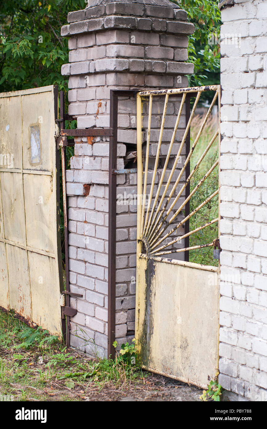 Ancienne grille rouillée et branlante guichet jaune métal avec une serrure entre les deux piliers en brique. Banque D'Images