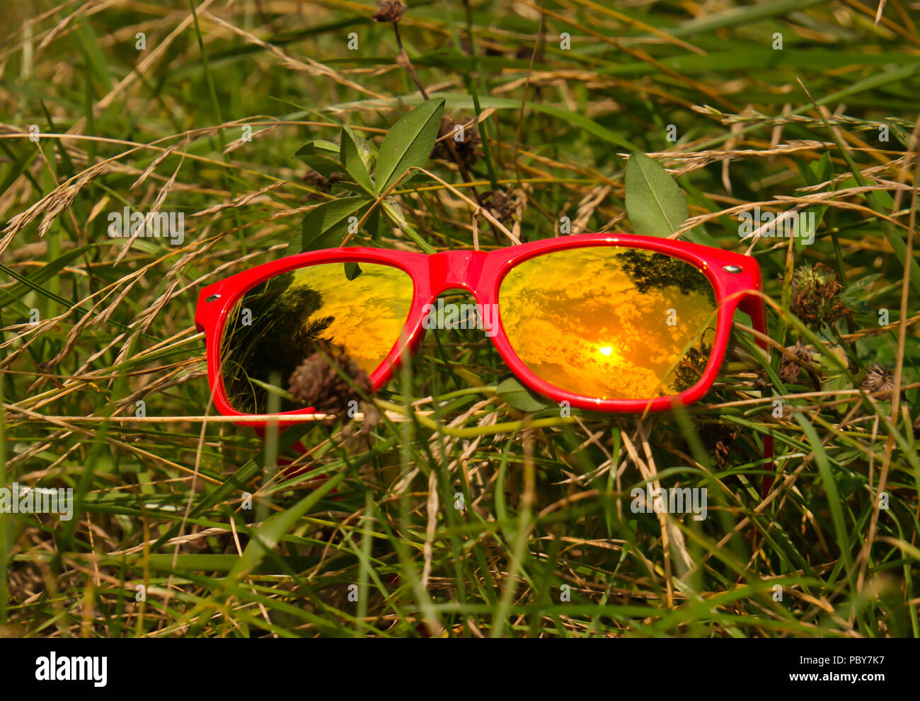 Nuages et soleil reflet dans le verre des lunettes de soleil avec cadre en  plastique rouge sur un pré dans l'herbe Photo Stock - Alamy