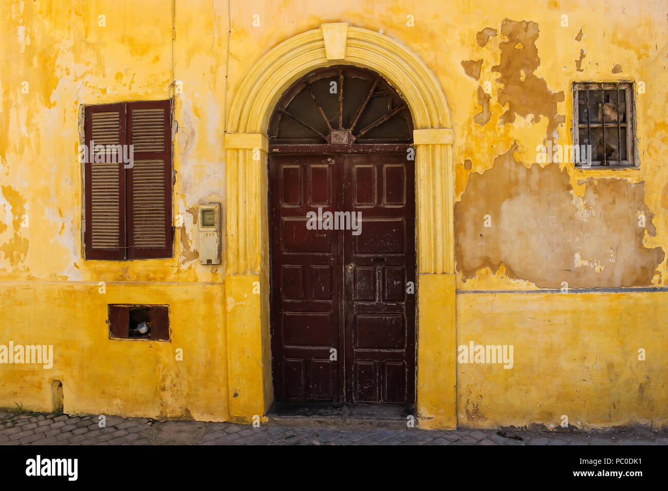 Vieux jaune façade d'une maison en bois avec porte brune avec un arc. Fenêtre avec un obturateur. Dans la rue ancienne forteresse portugaise à El Jadida, Maroc. Banque D'Images