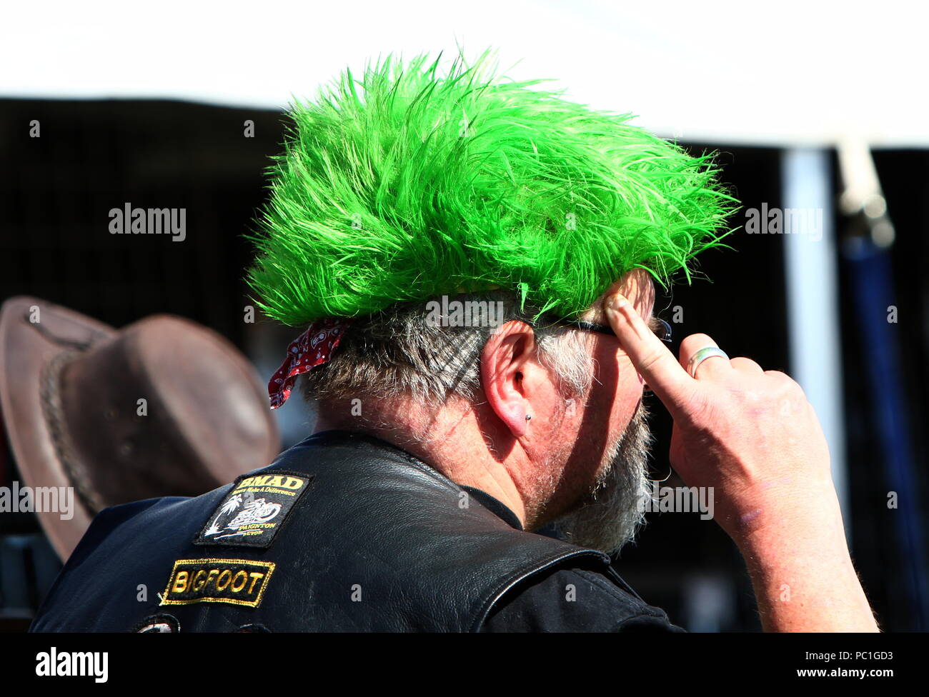 Paignton, Devon, Angleterre: Photo anonyme d'un motard avec une perruque verte faisant un geste du doigt vers son temple. À utiliser comme un concept, c'est-à-dire « utiliser votre cerveau » ? Banque D'Images