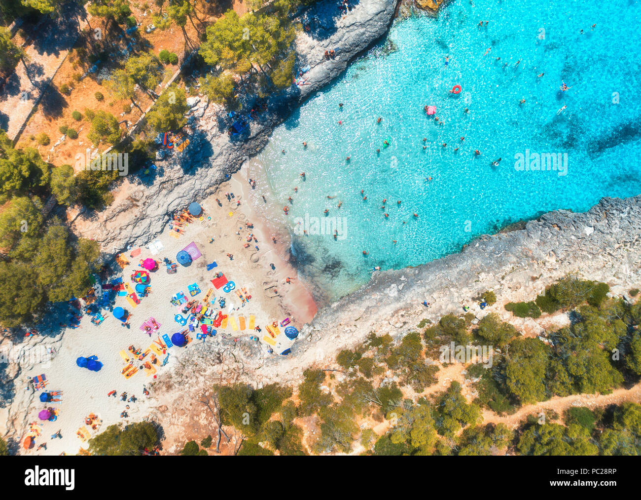 Vue aérienne de la plage de sable fin avec parasols colorés, d'une personnes dans la baie de la mer d'un bleu transparent avec l'eau et les arbres au lever du soleil en été. Billet d'en M Banque D'Images