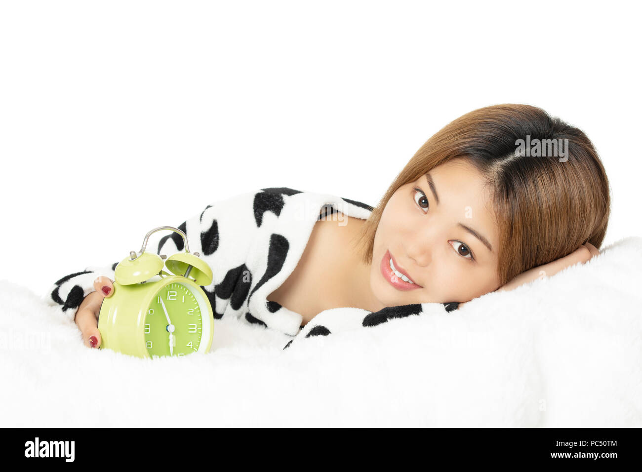 Femme chinoise au lit vêtu de noir et blanc pyjama avec réveil vert isolé sur fond blanc Banque D'Images