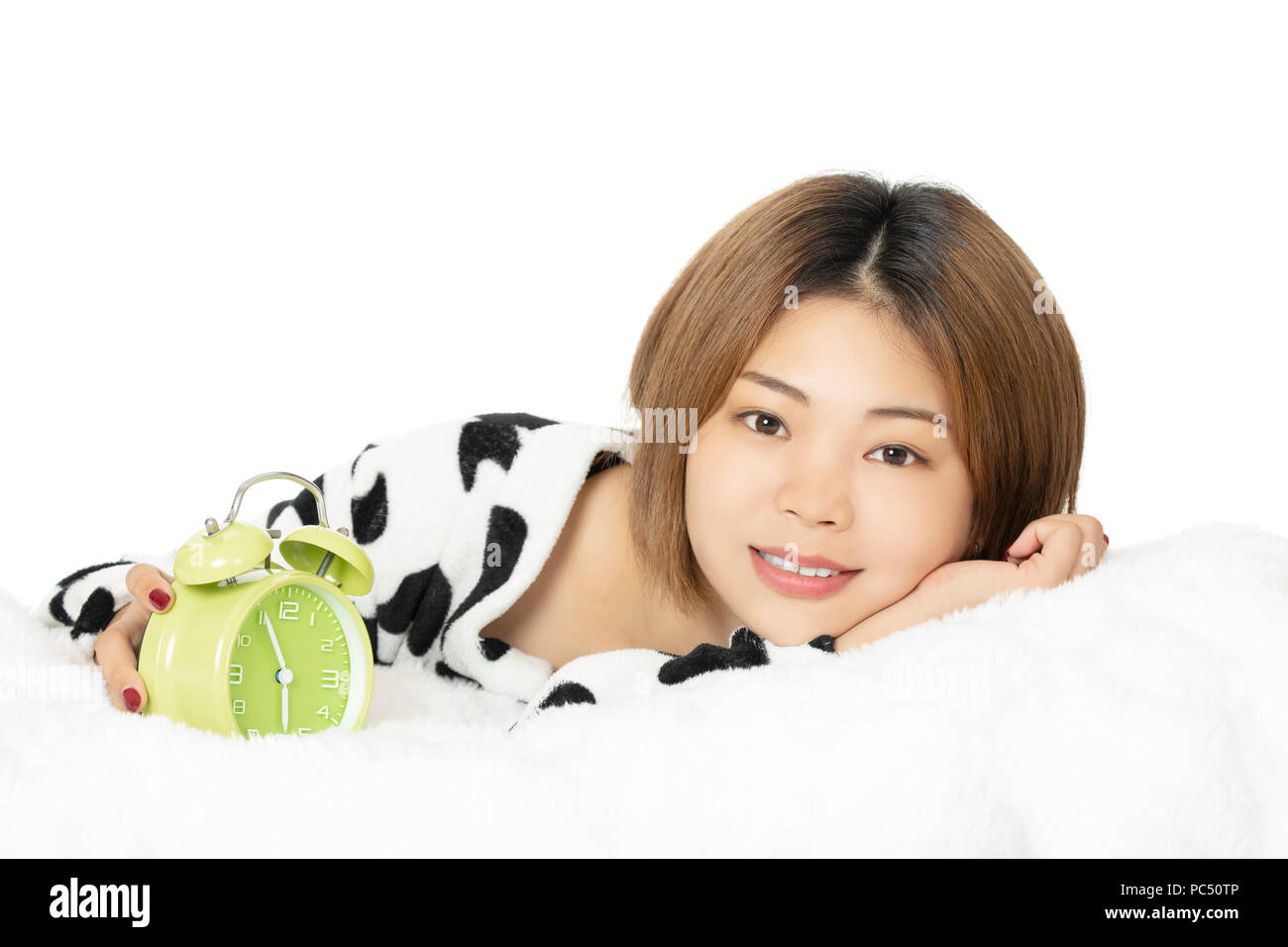 Femme chinoise au lit vêtu de noir et blanc pyjama avec réveil vert isolé sur fond blanc Banque D'Images