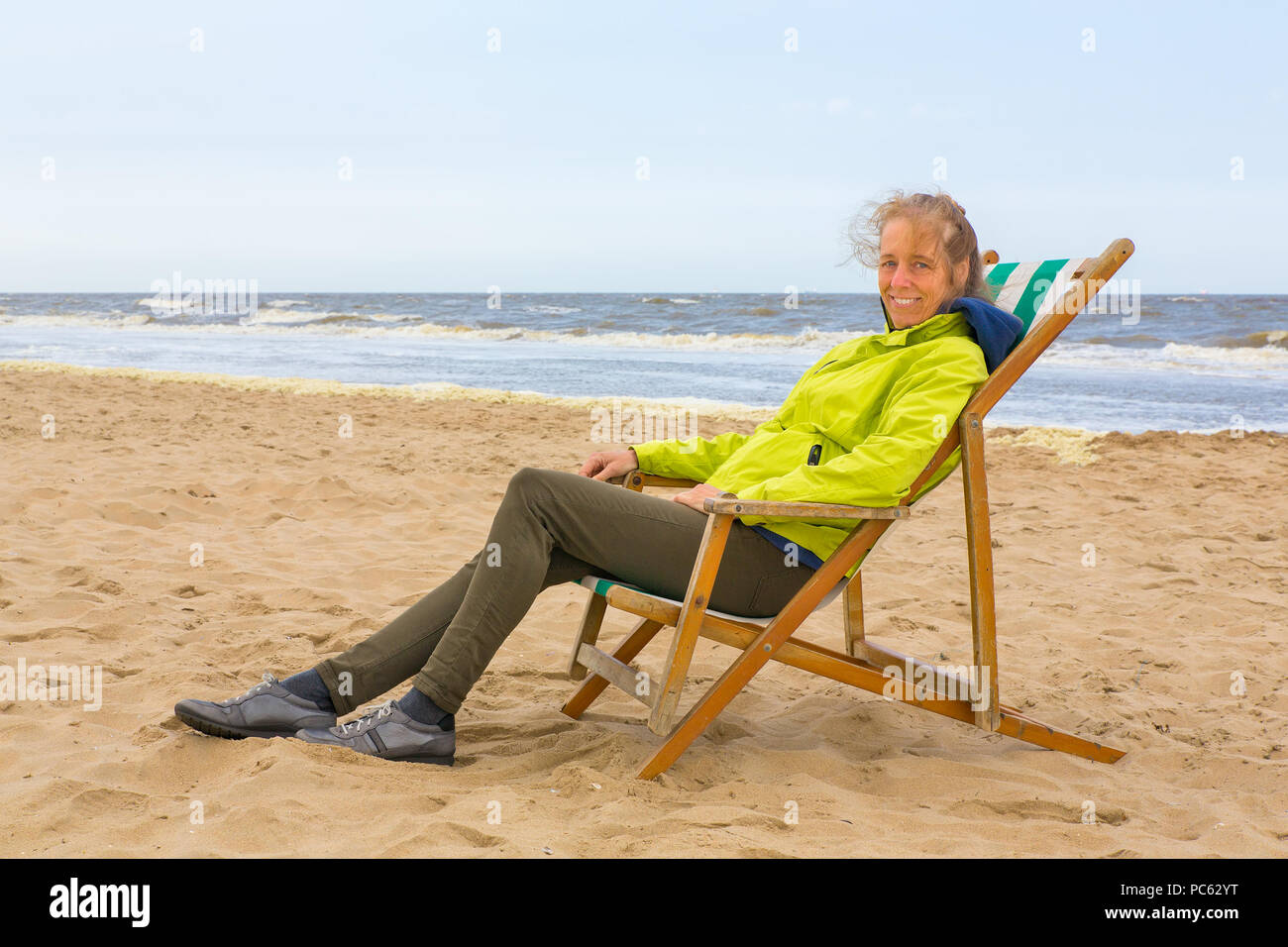 Caucasian woman avec veste d'été assis dans la chaise de plage par la mer Banque D'Images