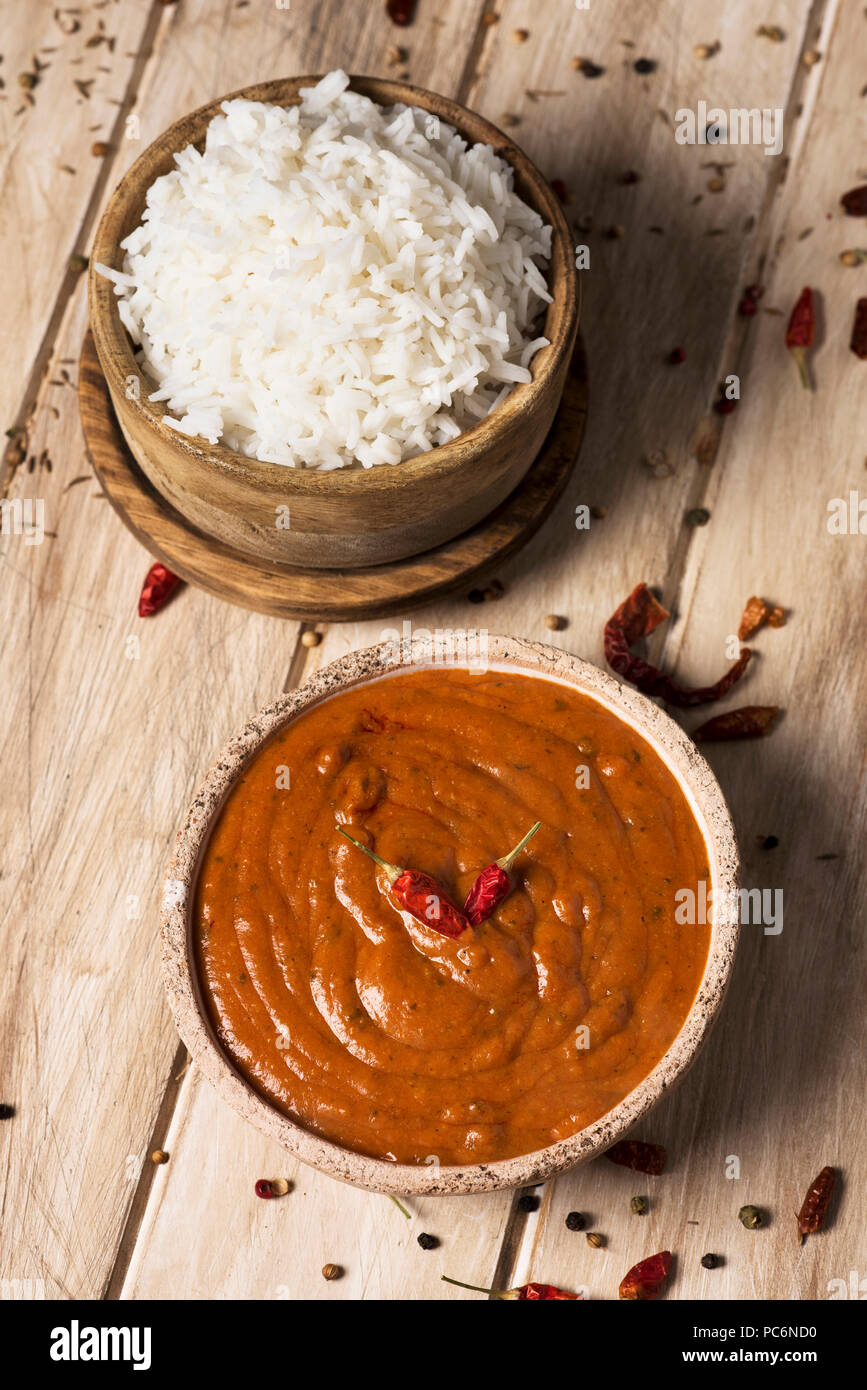 Portrait d'un bol avec un poulet korma curry et un bol avec du riz cuit sur une table en bois blanc Banque D'Images