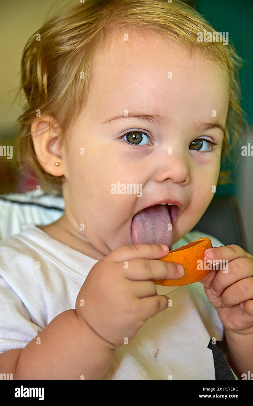Baby Girl eating orange pour la première fois. Montrant ses réactions drôles alors qu'elle goûte les fruits. Banque D'Images