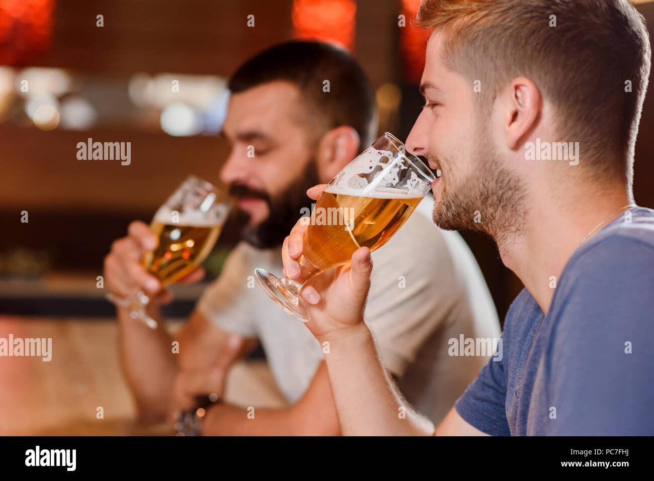 Vue latérale des deux hommes barbus tenant des verres de bière savoureuse et de boire. Deux joyeux amis assis dans un café ou un restaurant et s'amuser. Concept de gastronomie et de loisirs. Banque D'Images