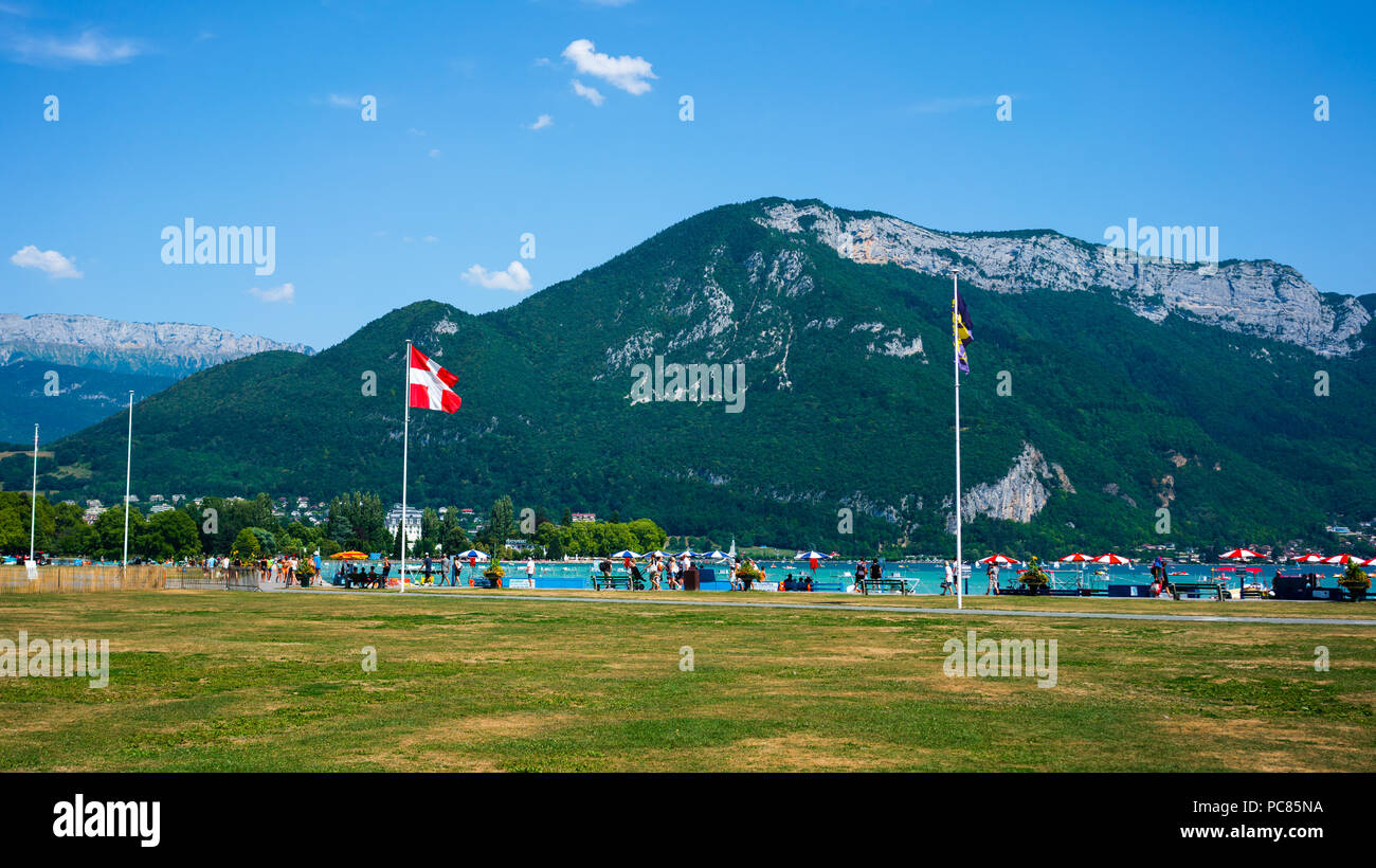 Les gens autour du lac d'Annecy rive avec Savoie drapeau région et Veyrier mont des Alpes montagnes en arrière-plan Banque D'Images