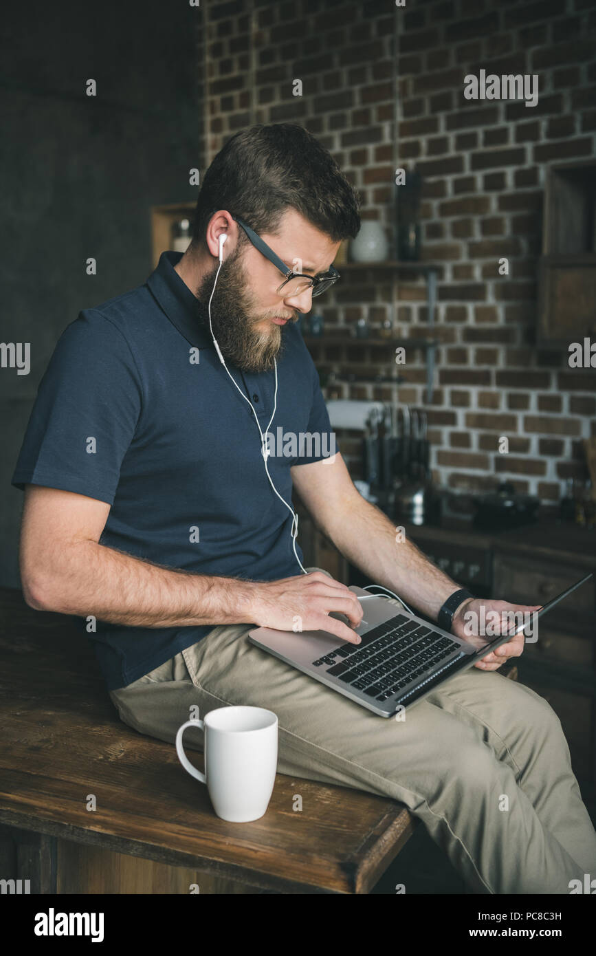 Jeune homme dans les verres à l'aide d'ordinateur portable et l'écoute la musique à la maison Banque D'Images