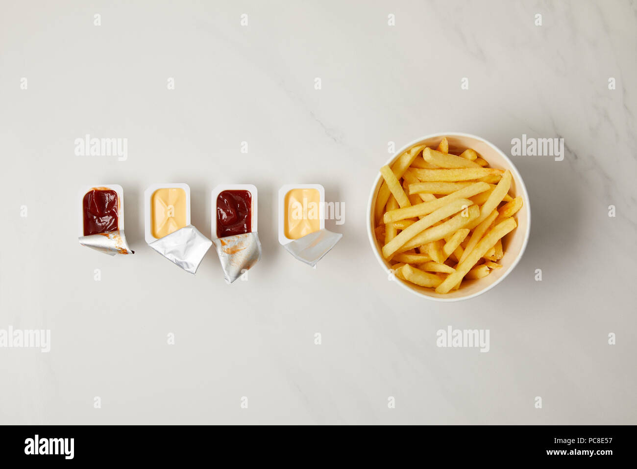 Vue de dessus de frites dans un bol avec des conteneurs de sauces dans la rangée on white Banque D'Images