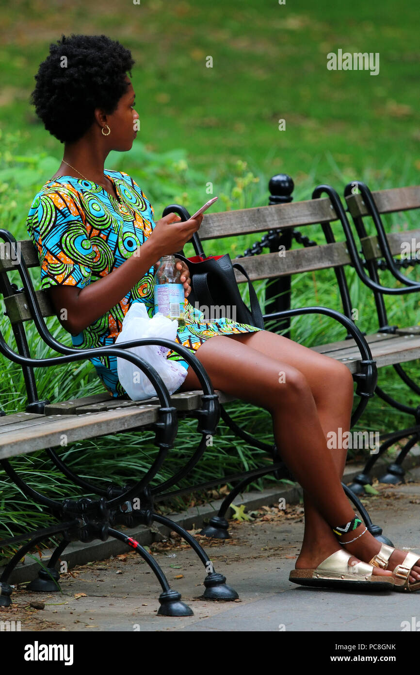 NEW YORK, NY - 10 juillet : Jeune femme noire sur un banc sur une chaude journée d'été à Washington Square Park à Manhattan le 10 juillet 2017 à New York, USA. Banque D'Images