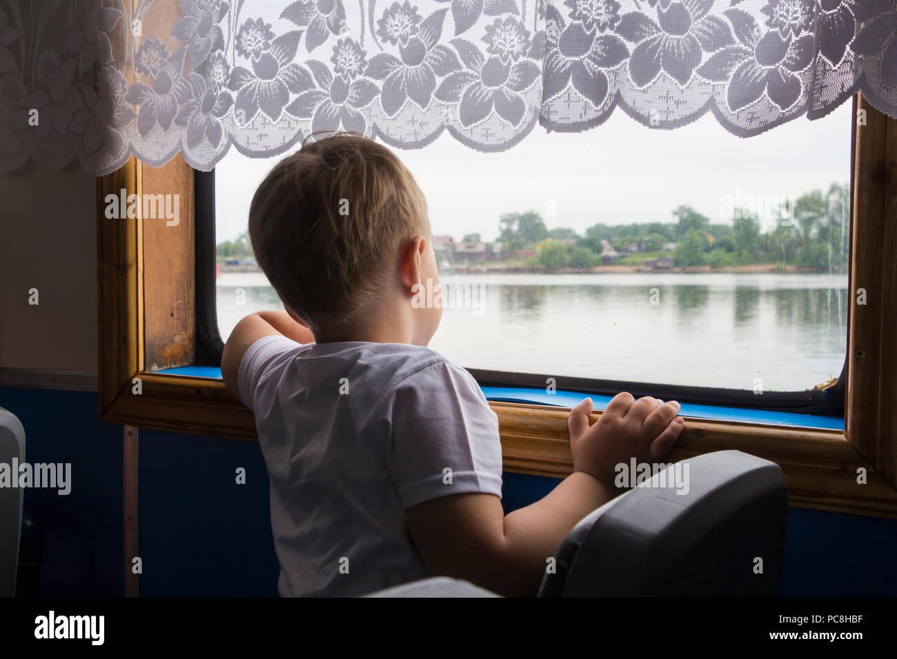 Un garçon regarde à travers les fenêtres à la rivière Banque D'Images