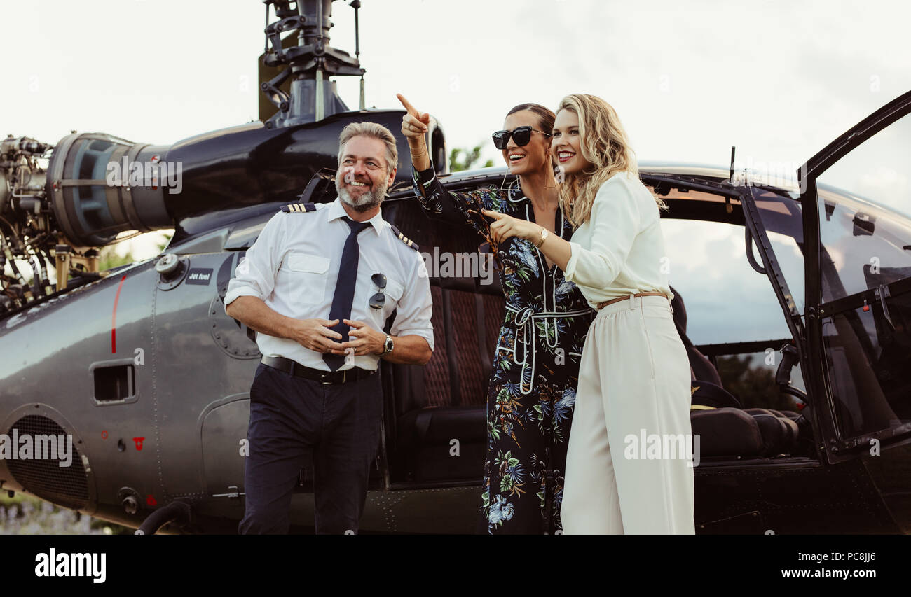 Belle femme debout à l'extérieur d'un hélicoptère avec pilote et du doigt quelque chose d'intéressant. Smiling women quitte un hélicoptère privé avec Banque D'Images