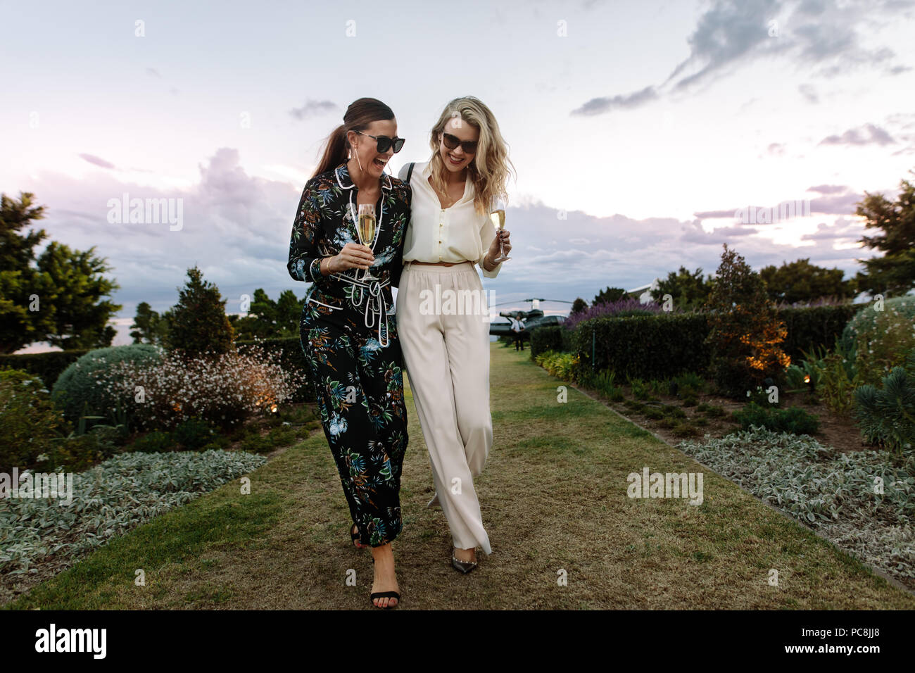 Les femmes à la mode de pleine longueur à marcher ensemble et rire à l'extérieur. Les femmes amis avec un verre de vin s'amuser en plein air. Banque D'Images