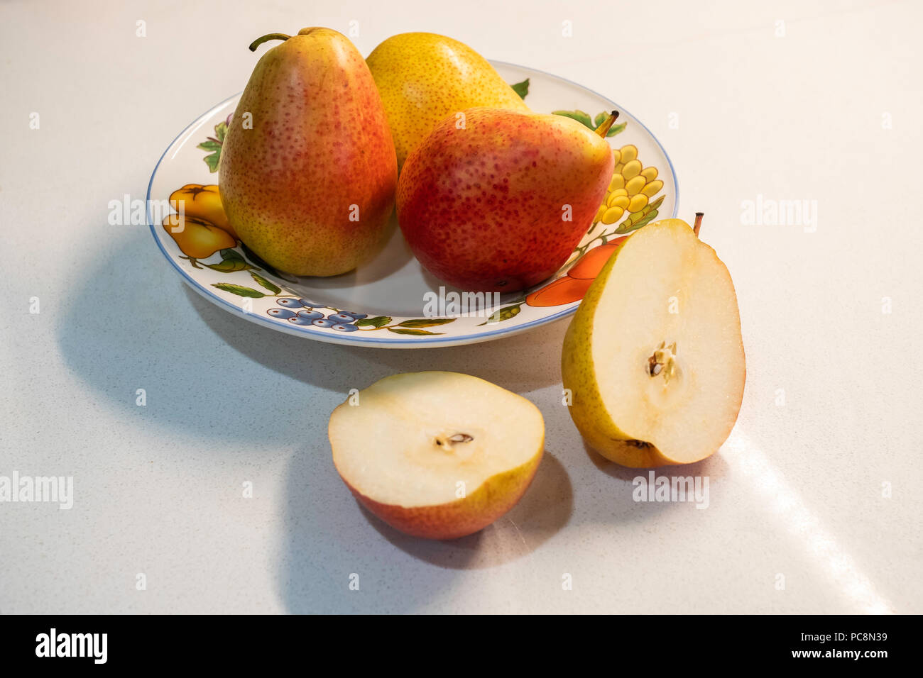 Ensemble de trois Poires Bartlett, Pyrus communis, dans un plat décoratif, une poire coupée en deux. fond blanc du comptoir. Banque D'Images