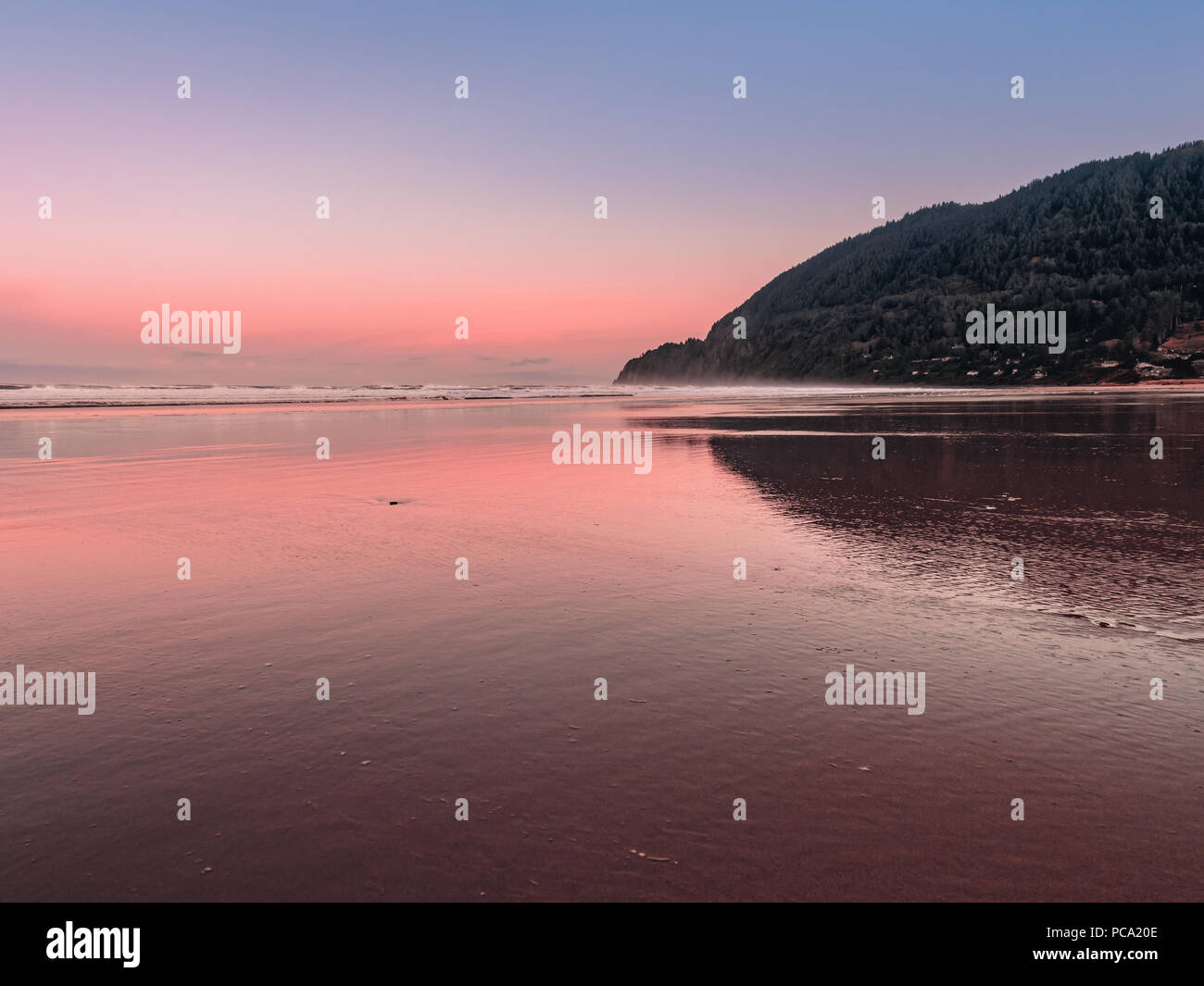 Vue paysage de montagne à partir de Manzanita Neahkahnie Beach sur la côte Pacifique du nord de l'Oregon. Joli ciel rose réfléchissant sur le sable humide. Banque D'Images