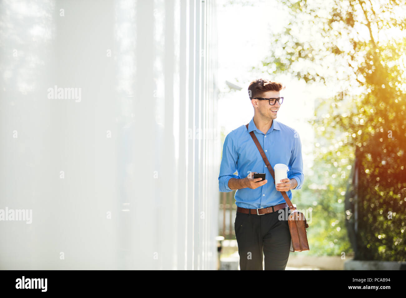 Beau jeune homme de se rendre au travail, au bureau, en chemise bleue avec un café dans les mains sur une journée ensoleillée Banque D'Images