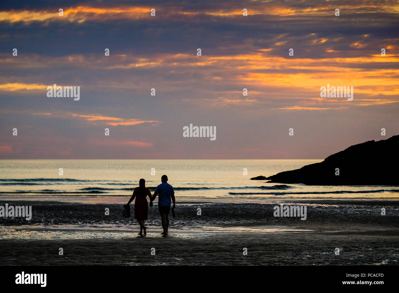 Couple en train de marcher sur la plage de Porth Newquay Cornwall au en au coucher du soleil Banque D'Images