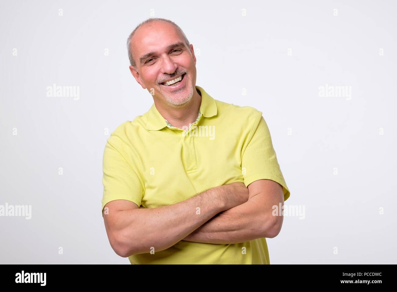 Beau charmant homme mûr dans l'usure jaune occasionnels en gardant les bras croisés et sourire Banque D'Images