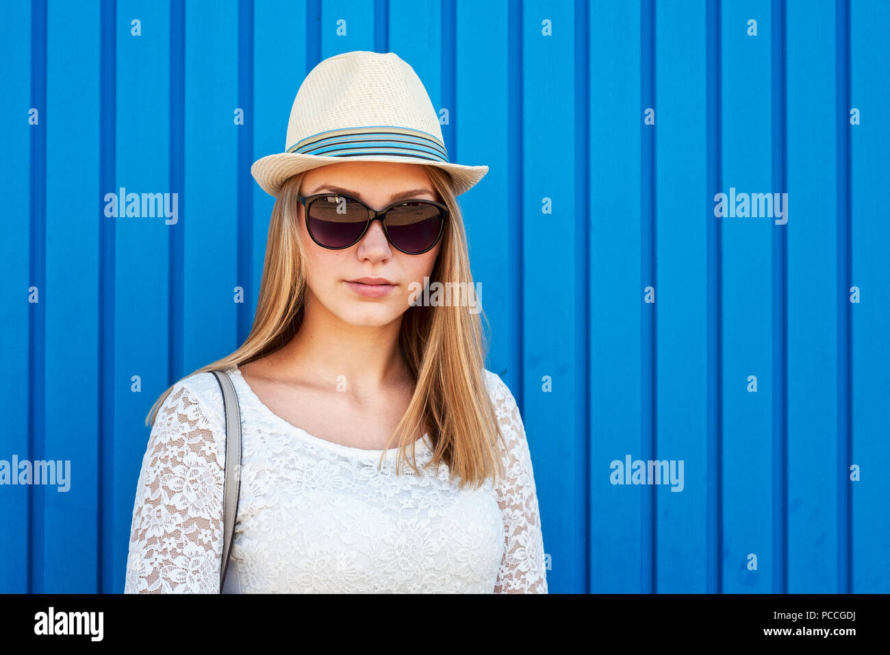 De vie de plein air portrait de jeune fille hipster avec de longs cheveux blonds, des lunettes et un chapeau posant sur fond bleu Banque D'Images