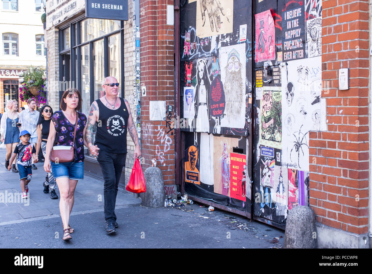 Punk rock masculin senior man holding hands with partner marcher en face de mur recouvert de peintures murales art de rue et des affiches dans la rue commerciale, à l'avant Banque D'Images