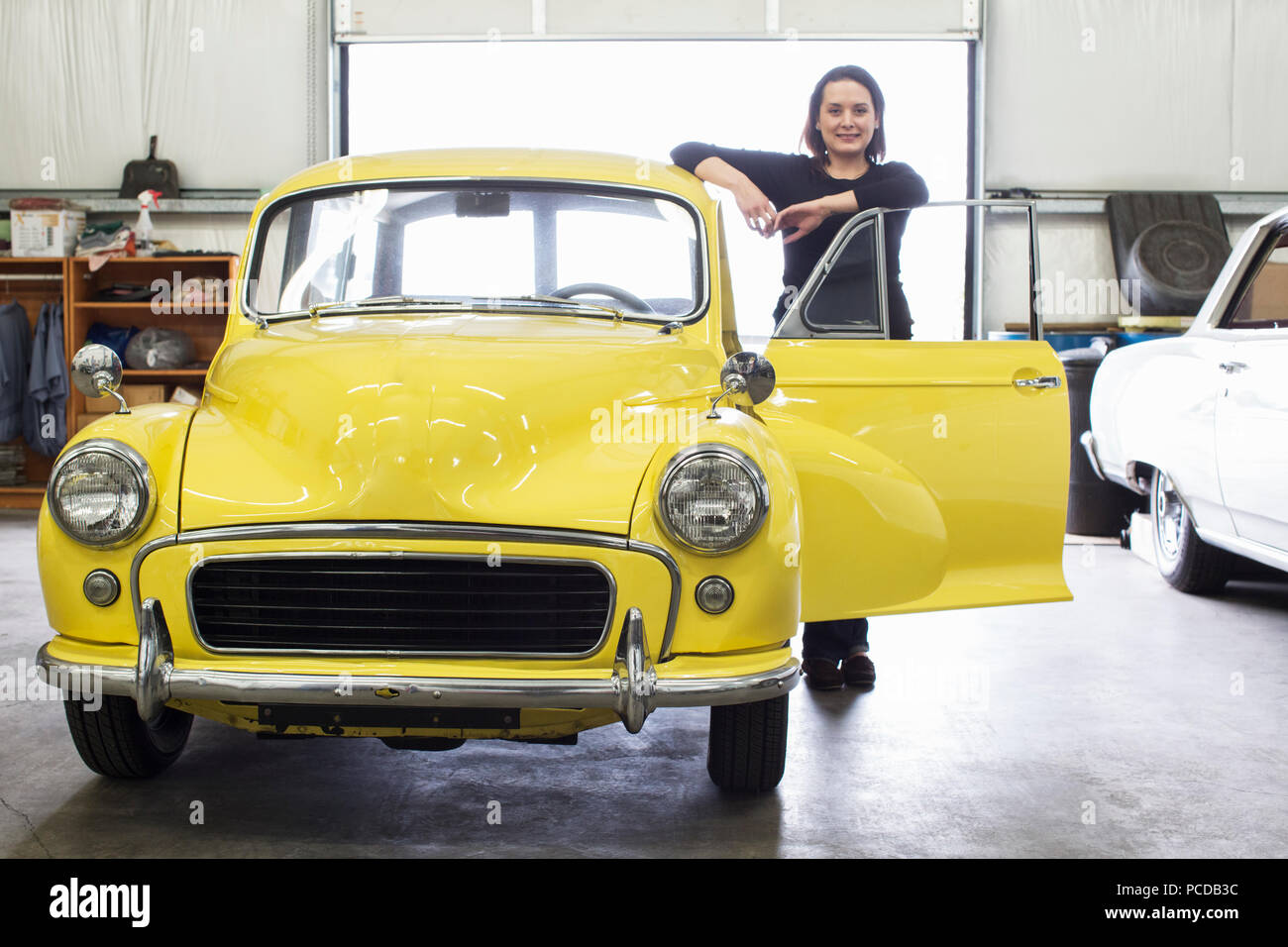 Une femme de race blanche se trouve à côté de sa vieille voiture dans une voiture classique atelier de réparation. Banque D'Images