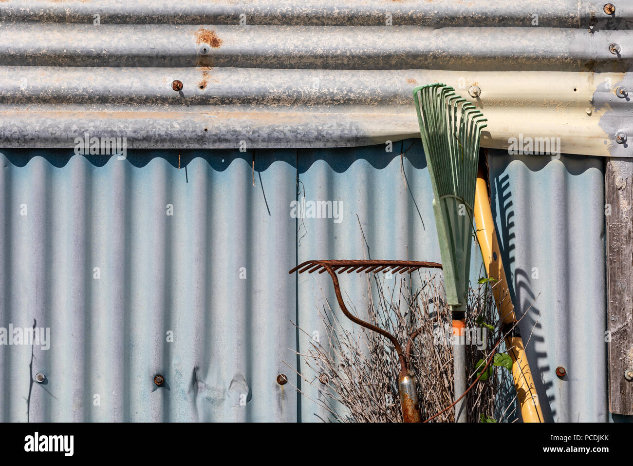 Râteaux appuyé contre un mur de métal ondulé ; Ginowan, Okinawa, Japon Banque D'Images