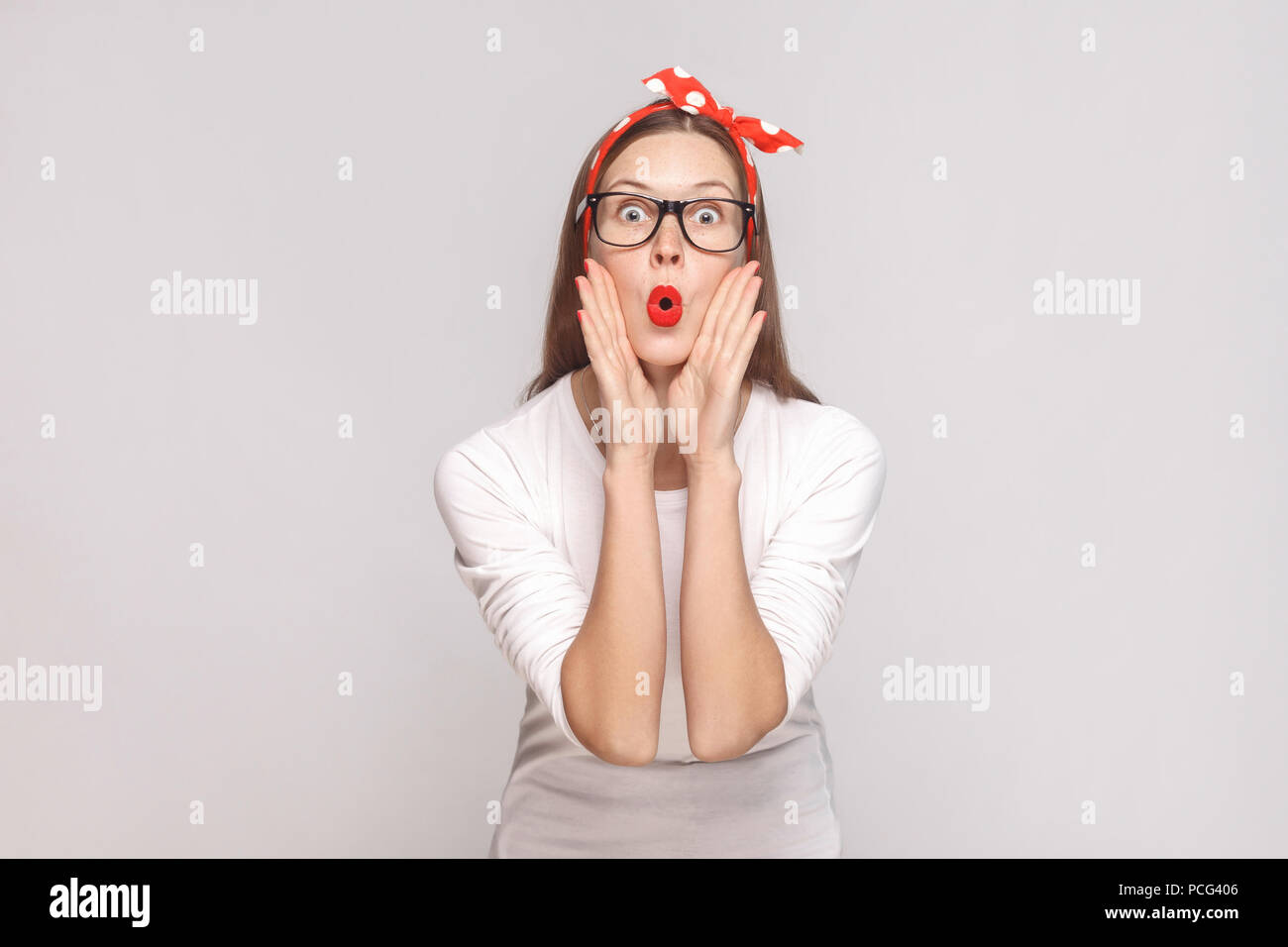 De grands yeux surpris portrait de belle jeune femme émotionnelle en t-shirt blanc avec des taches de rousseur, lunettes noires, rouge lèvres et head. Piscine studio sh Banque D'Images